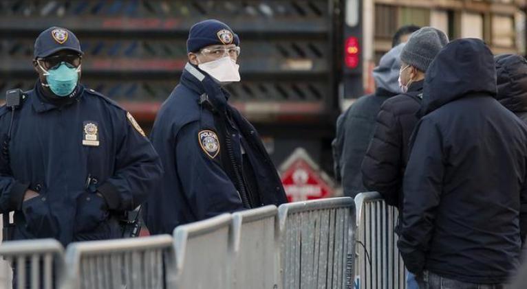 Policías de la ciudad de Nueva York utilizan máscarillas mientras observan a personas que hacen fila para realizarse pruebas por coronavirus fuera del Hospital Center, en el vecindario de Queens, Nueva York, EEUU, Marzo 26, 2020. REUTERS/Stefan Jeremiah
